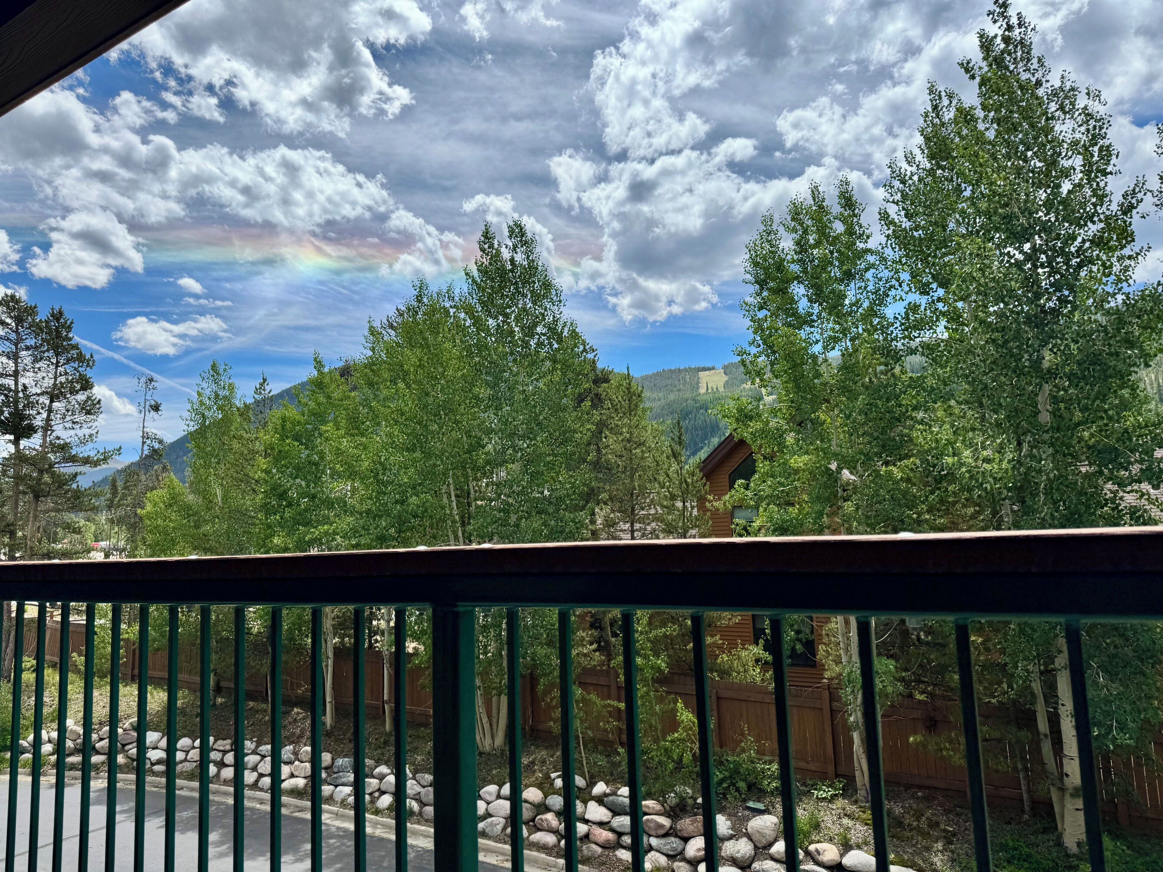 Vista de un paisaje verde y exuberante con una cabaña de madera y un arcoíris en el cielo.