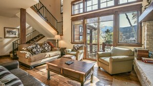 A spacious living room with a high ceiling, a staircase, and large windows offering a view of the outdoors. - Keystone Sanctuary 248 by SummitCove Vacation Lodging (Keystone)