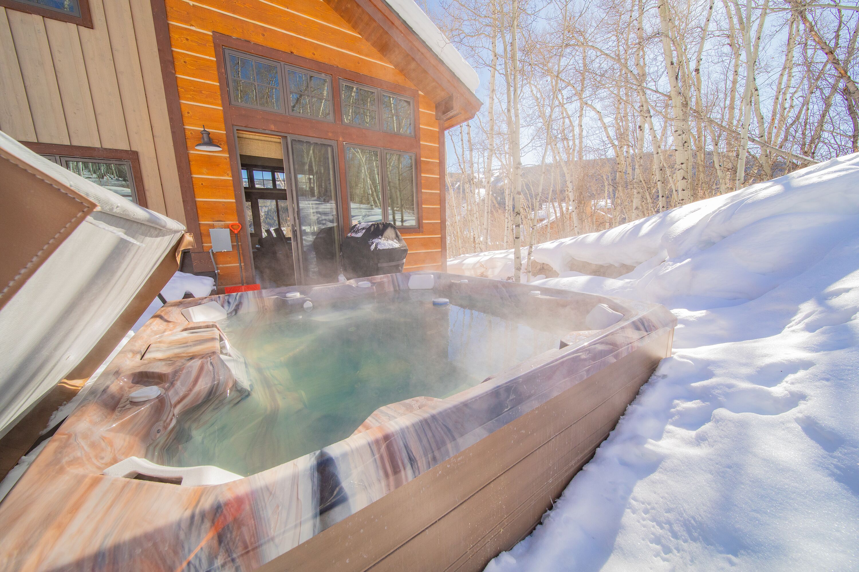 A hot tub in a snowy outdoor area with a wooden cabin in the background.