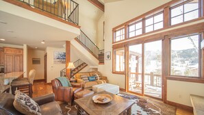 A spacious living room with a high ceiling, a staircase, and large windows offering a view of the outdoors. - Keystone Sanctuary 248 by SummitCove Vacation Lodging (Keystone)