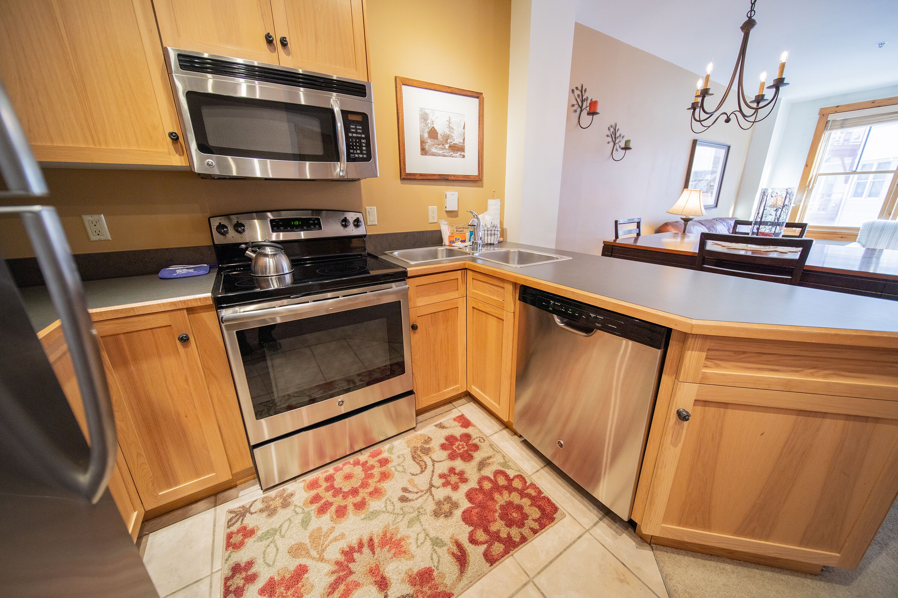 A modern kitchen with stainless steel appliances, wooden cabinets, a large island, and a floral rug.