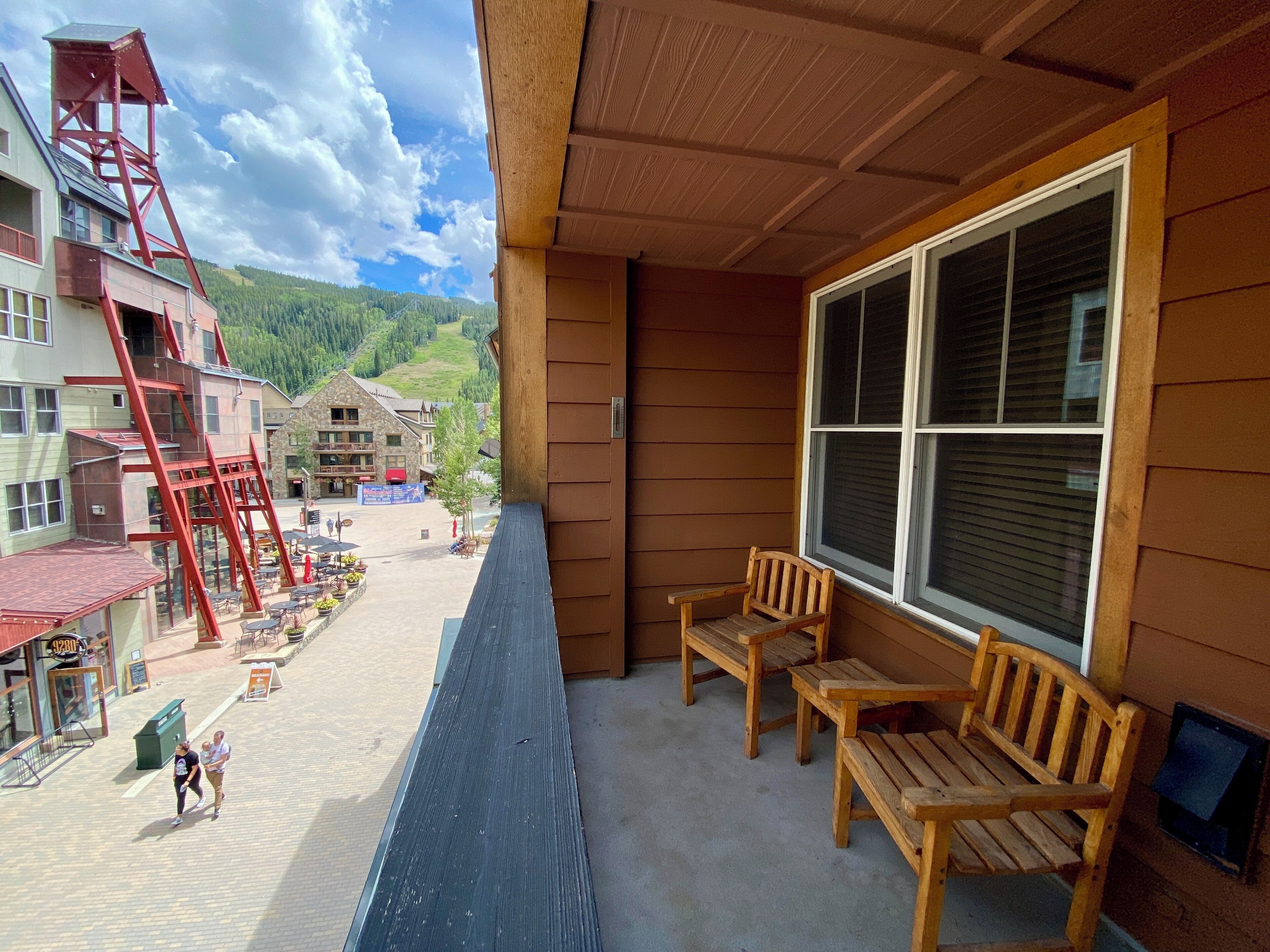 A balcony with wooden benches and a large window overlooking a town square with buildings and a mountain in the background.