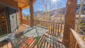 A wooden deck with a glass table and chairs, overlooking a mountainous landscape. - Hidden River Lodge 5979 (Keystone)
