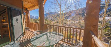 A wooden deck with a glass table and chairs, overlooking a mountainous landscape.