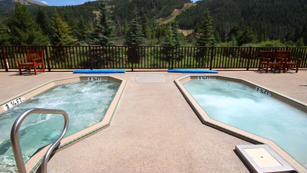 Un área de piscina con dos jacuzzis, una terraza de madera y vistas a una montaña boscosa.