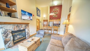 A living room with a stone fireplace, a wooden coffee table, a beige sofa, and a dining area with a chandelier. - Hidden River Lodge 5979 (Keystone)