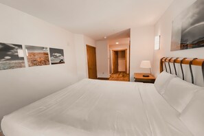 A hotel room with a large bed, a wooden headboard, a nightstand with a lamp, and a view of the hallway. - Expedition Station 8607 by SummitCove Vacation Lodging (Keystone)