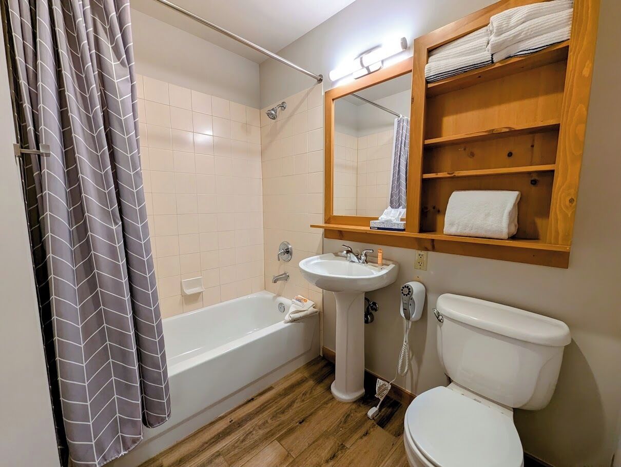 A bathroom with a bathtub, a sink, a toilet, and a wooden shelf with towels.
