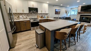 A modern kitchen with white cabinets, a large island with bar stools, a built-in oven, and a TV mounted above the island. - Liftside 14B (Keystone)