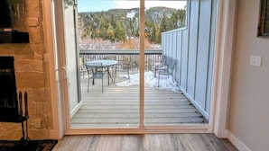 A sliding glass door leading to an outdoor patio with a table and chairs, a stone fireplace, and a view of a forested area. - Liftside 14B (Keystone)