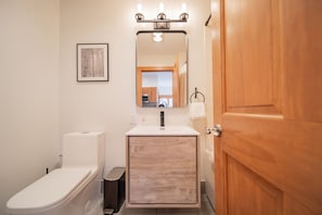 A bathroom with a white toilet, a wooden vanity with a mirror, and a wooden door.