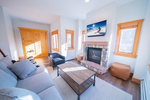 A living room with a sofa, a coffee table, a fireplace, and a television mounted above it.