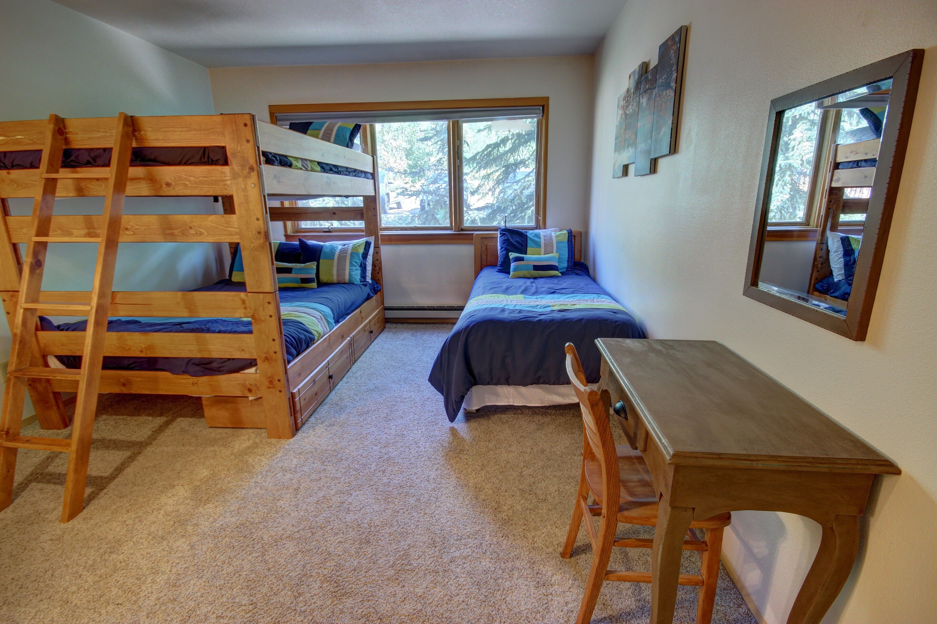 A bedroom with bunk beds, a desk, and a window with a view of trees.
