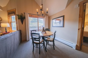 A dining area with a round table, four chairs, a chandelier, and a window with curtains. - Buffalo Lodge 8411 by SummitCove Vacation Lodging (Keystone)