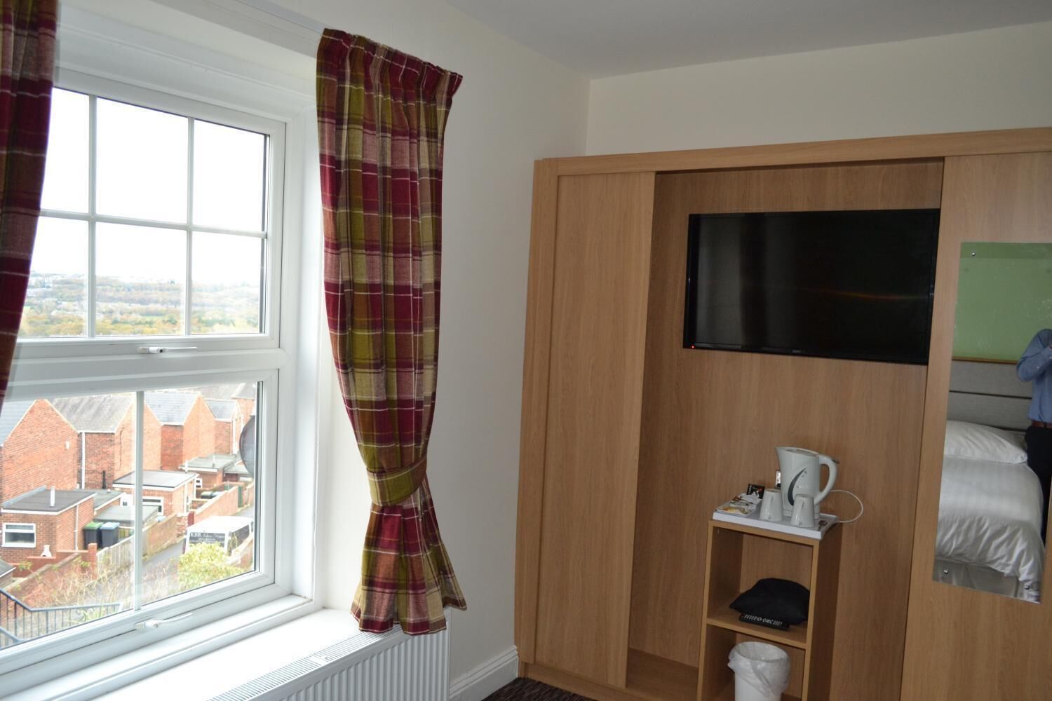 A bedroom with a window, a bed, a TV, and a small shelf with items.