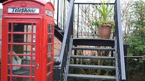 A red telephone booth with a sign that reads "Telephone" and a metal staircase leading up to a garden area with a potted plant. - Oak Tree Inn (Stanley)