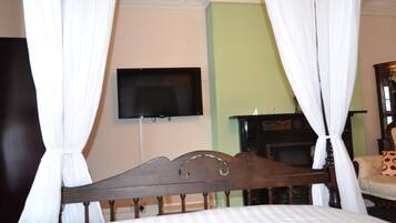 A bedroom with a four-poster bed, a television mounted on the wall, and a fireplace.