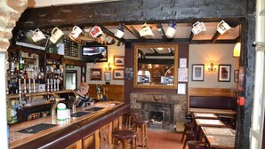 A bar area with a counter, stools, a television, and a fireplace. - Oak Tree Inn (Stanley)
