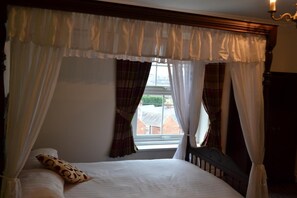 Un dormitorio con cama de dos columnas, ropa de cama blanca y cortinas a cuadros.