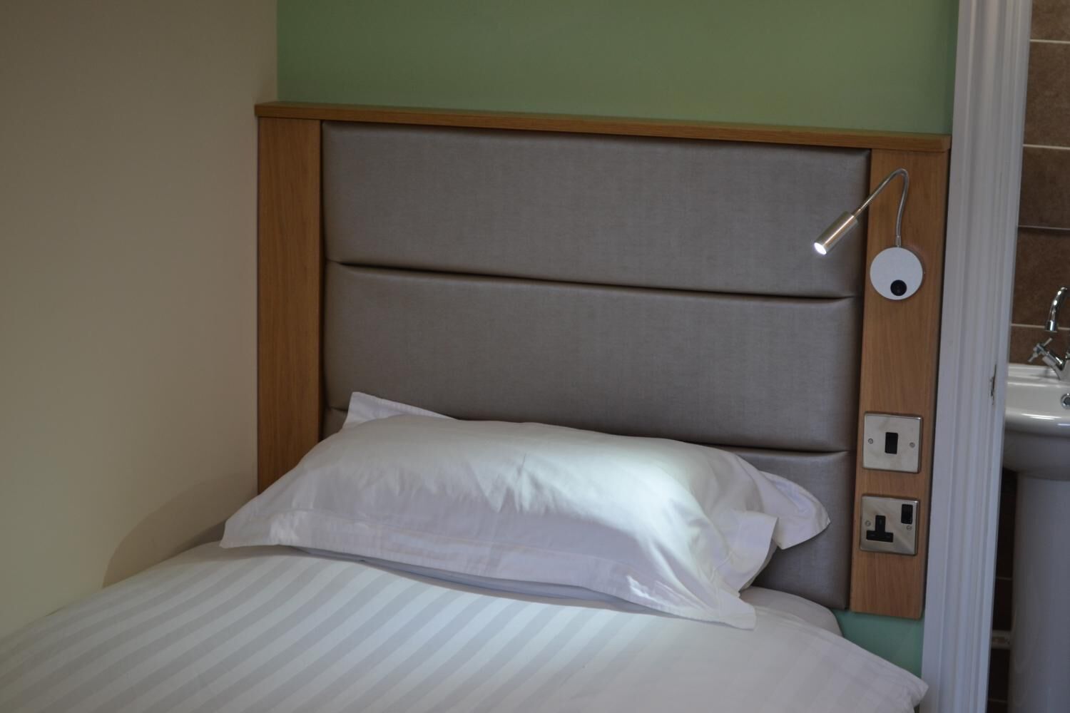 Una cama con cabecera, ropa de cama blanca y una lámpara de noche.