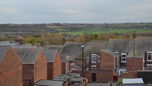 A residential area with brick houses, a clear view of the surrounding countryside, and a distant town.