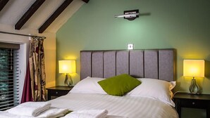 A neatly made bed with white linens and a green pillow, two bedside lamps, and a window with curtains. - Oak Tree Inn (Stanley)