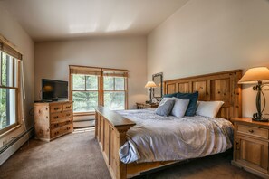 A bedroom with a wooden bed, a dresser, a TV, and a window with a view of trees. - Jack Pine 8008 by SummitCove Vacation Lodging (Keystone)