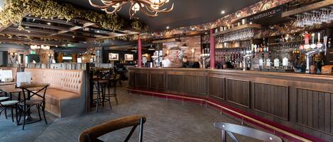 A bar area with a wooden counter, seating, and a chandelier.