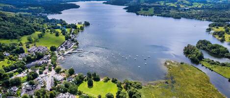 An aerial view of a coastal town with a marina, green landscapes, and a large body of water.