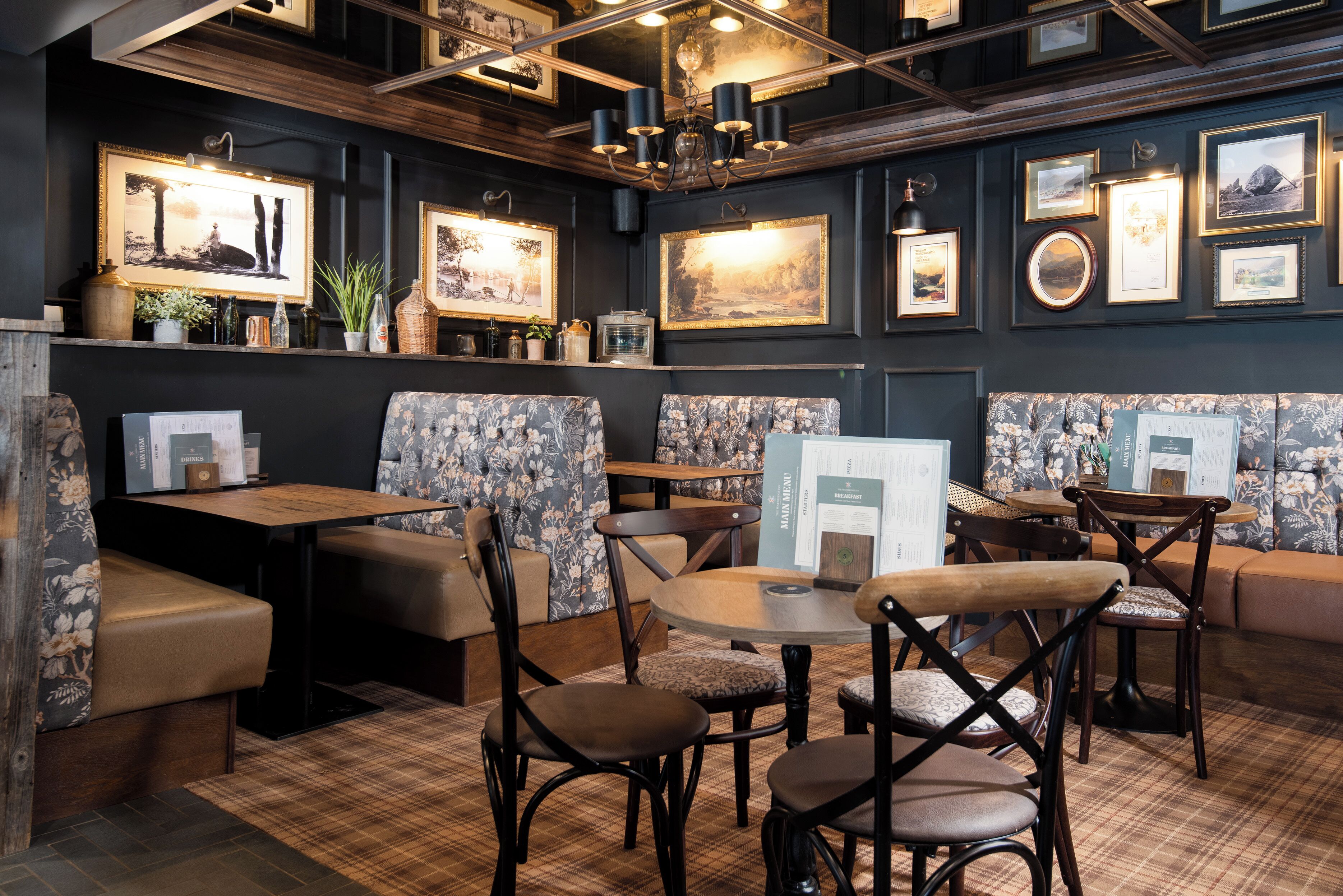 A cozy restaurant with wooden furniture, floral upholstery, and wall-mounted artwork.
