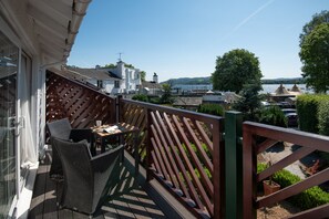 A balcony with wicker furniture, a view of a lake, and houses in the background.