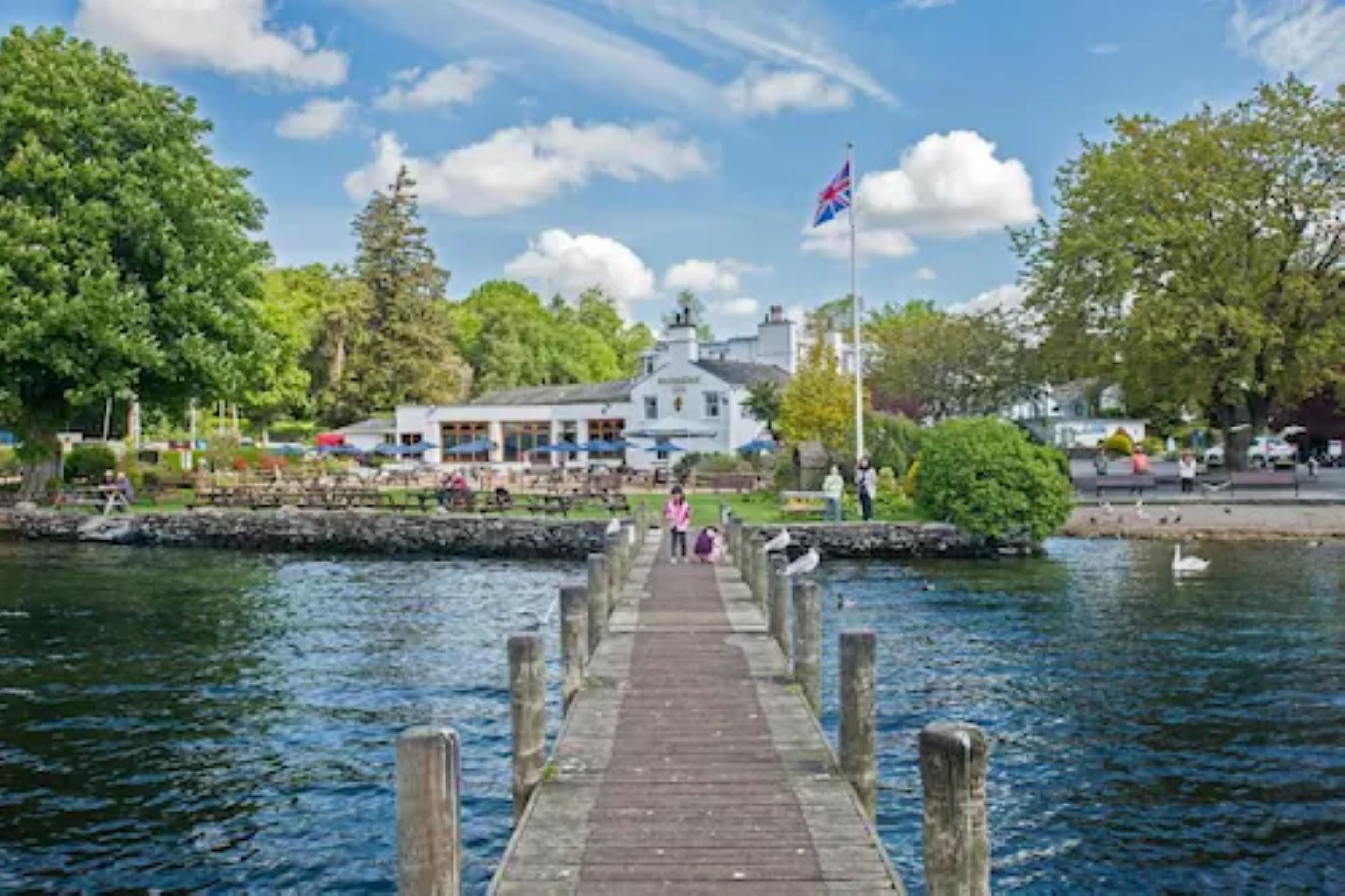 A wooden pier leading to a building with a flag, surrounded by water and greenery.