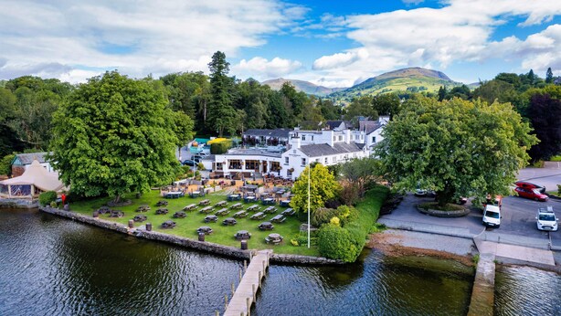 A riverside hotel with outdoor seating, a dock, and a view of the surrounding hills.