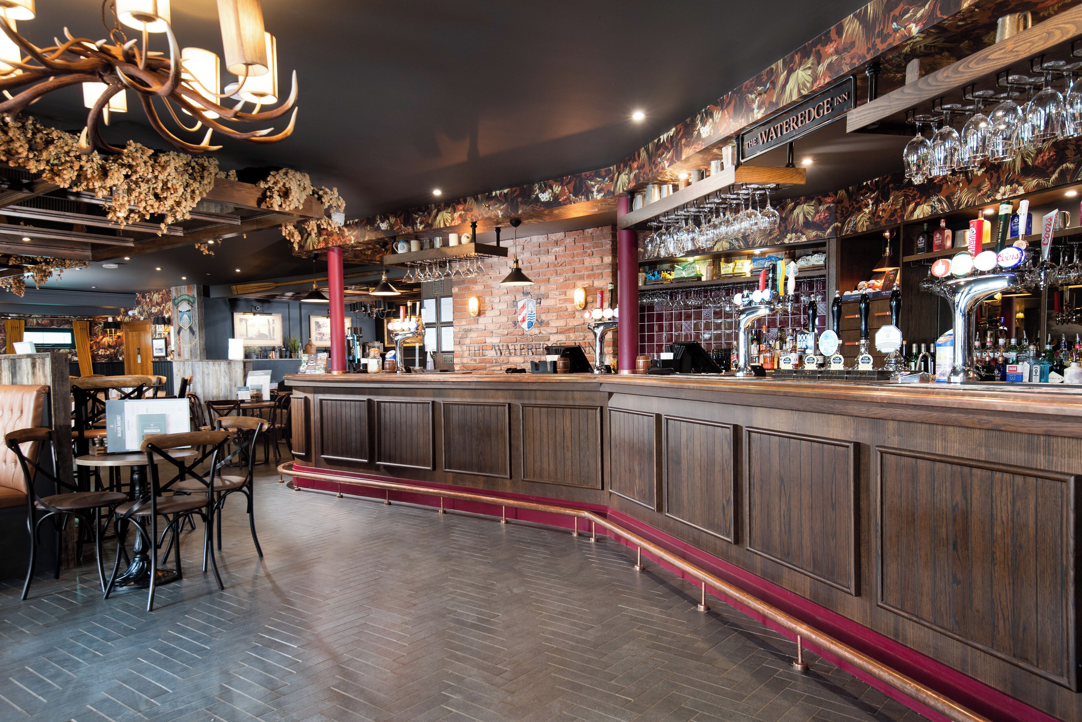 A bar area with wooden bar counters, seating, and a variety of bottles and glasses.