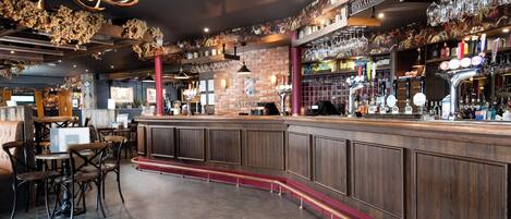 Zona de bar con mostradores de madera, asientos y una variedad de botellas y vasos.