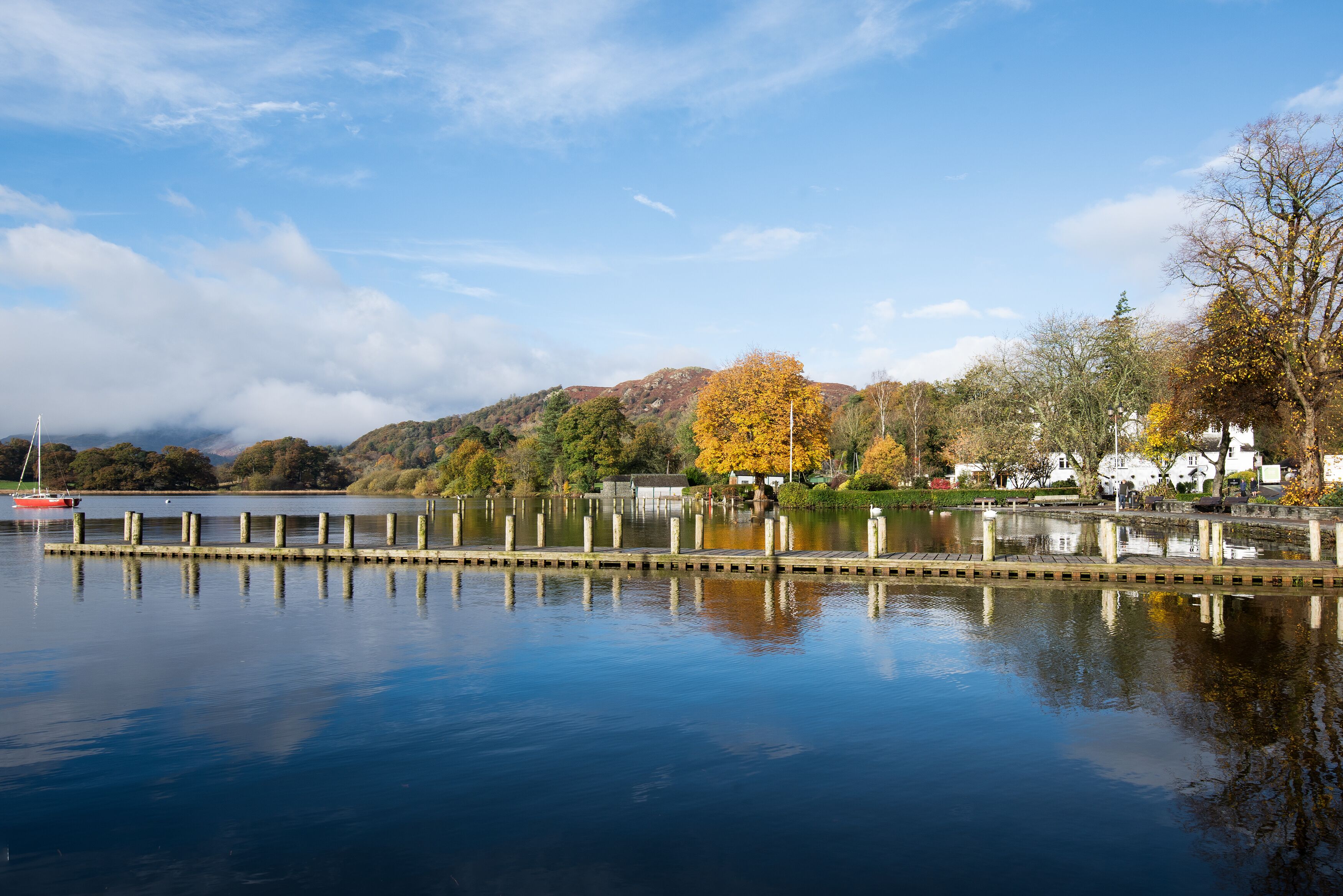 A calm lake with a dock, surrounded by autumn-colored trees and a mountain in the background.