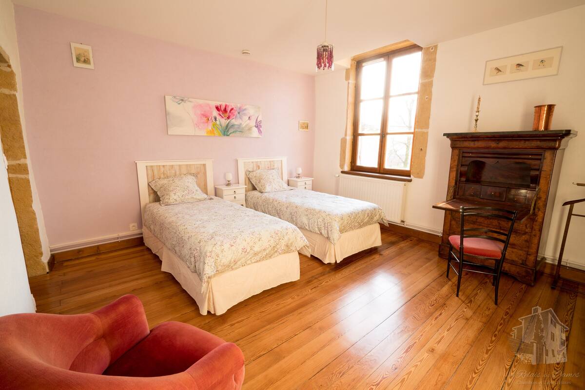 Un dormitorio con dos camas, piso de madera, una silla roja y una chimenea.