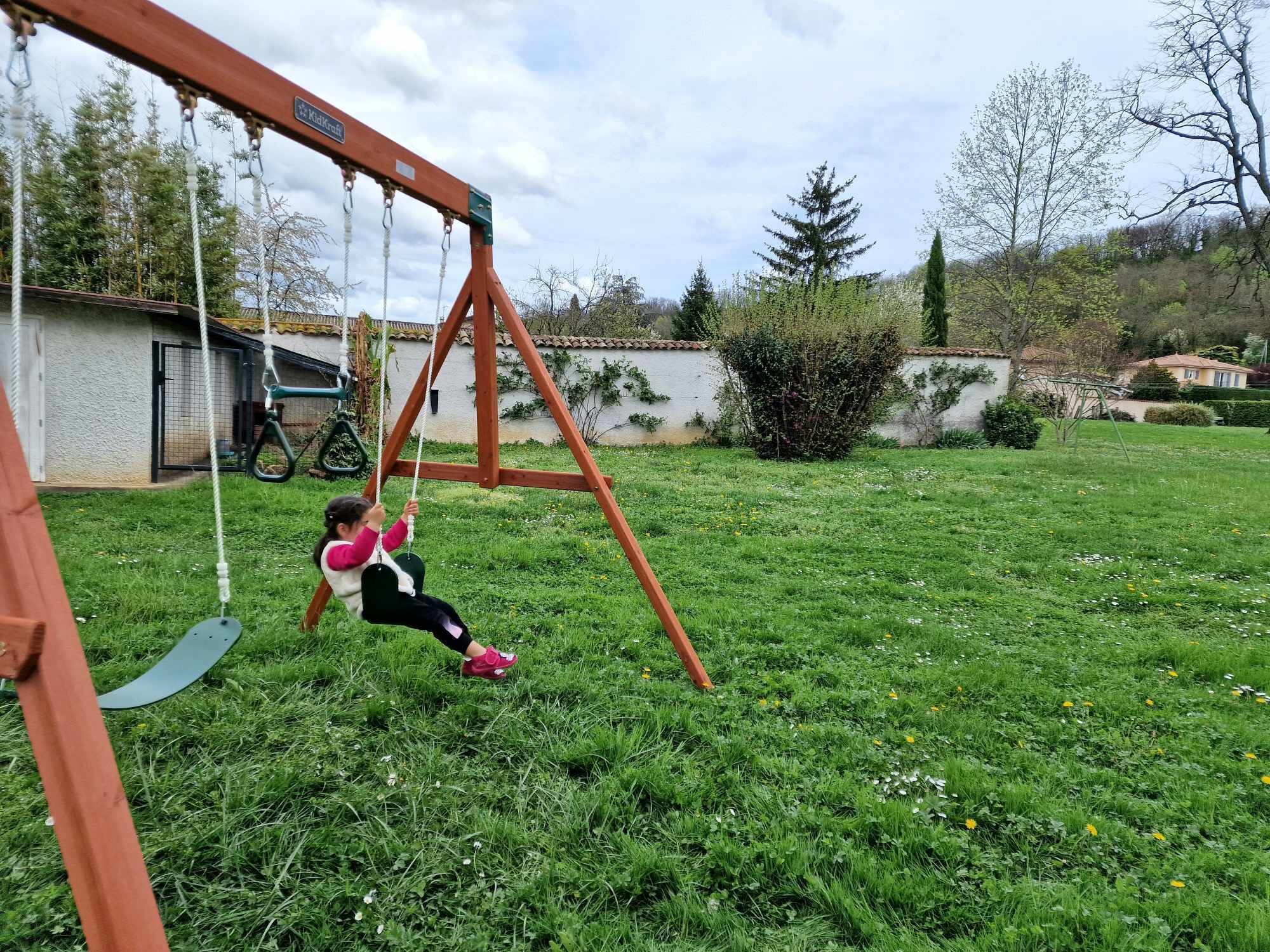 A child on a swing in a grassy backyard with a house and trees in the background.