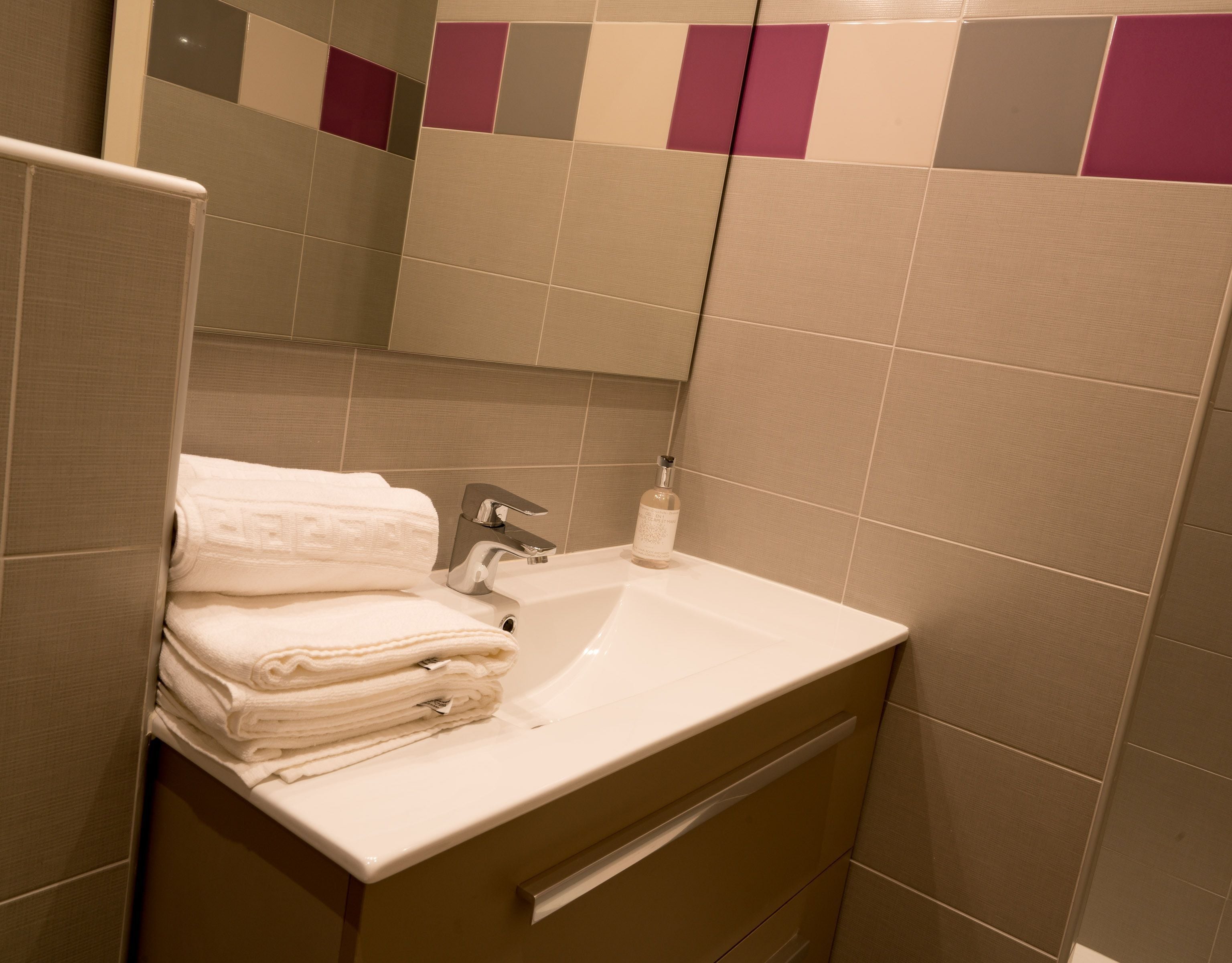 A bathroom with a sink, a mirror, and a towel stack.