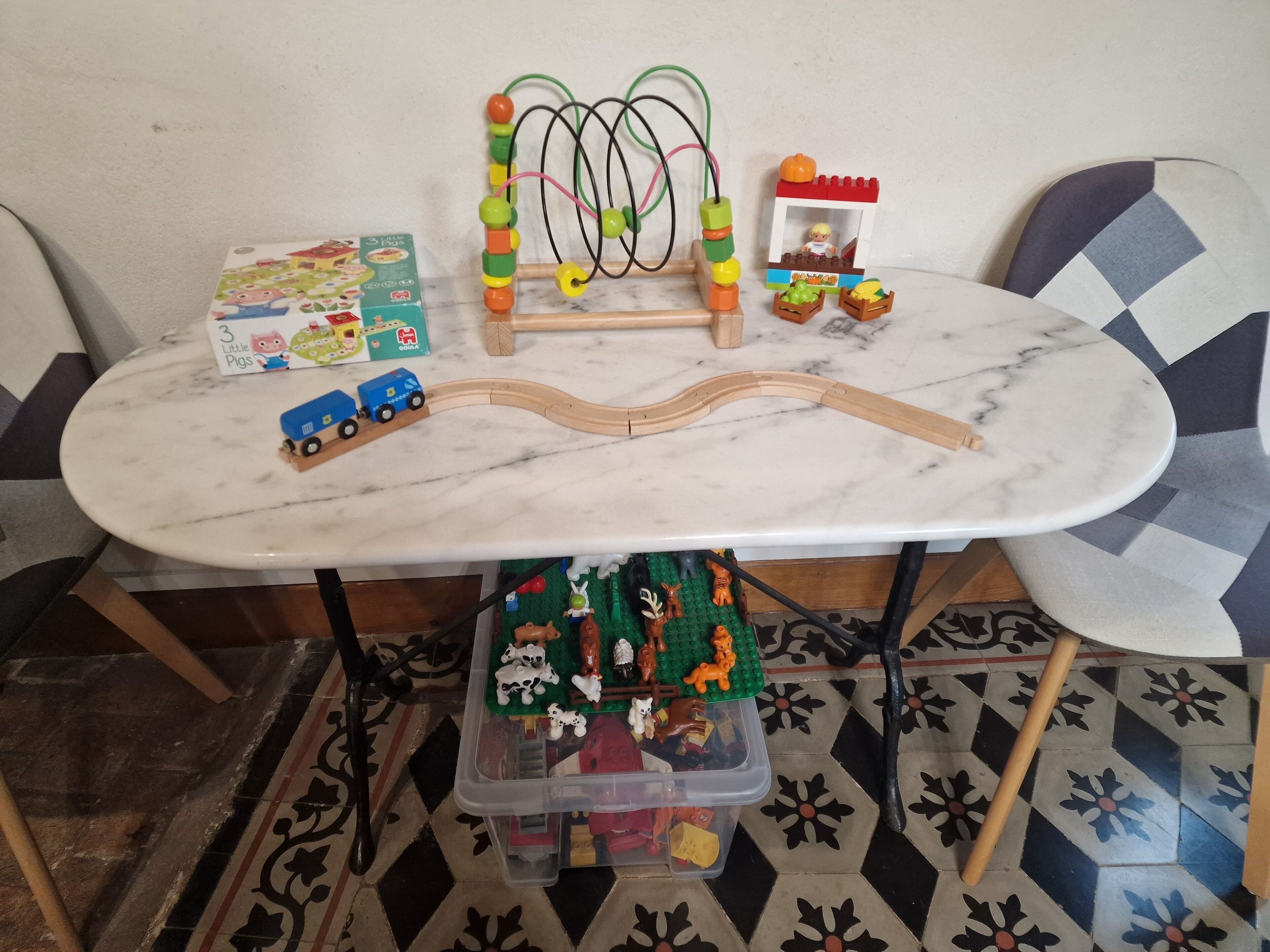 A marble table with a toy train set, a bead maze, and a toy farm.