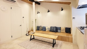 A compact living space with a wooden bench, a white door, and a kitchenette area. - SEKAI HOTEL Momiji (Osaka)