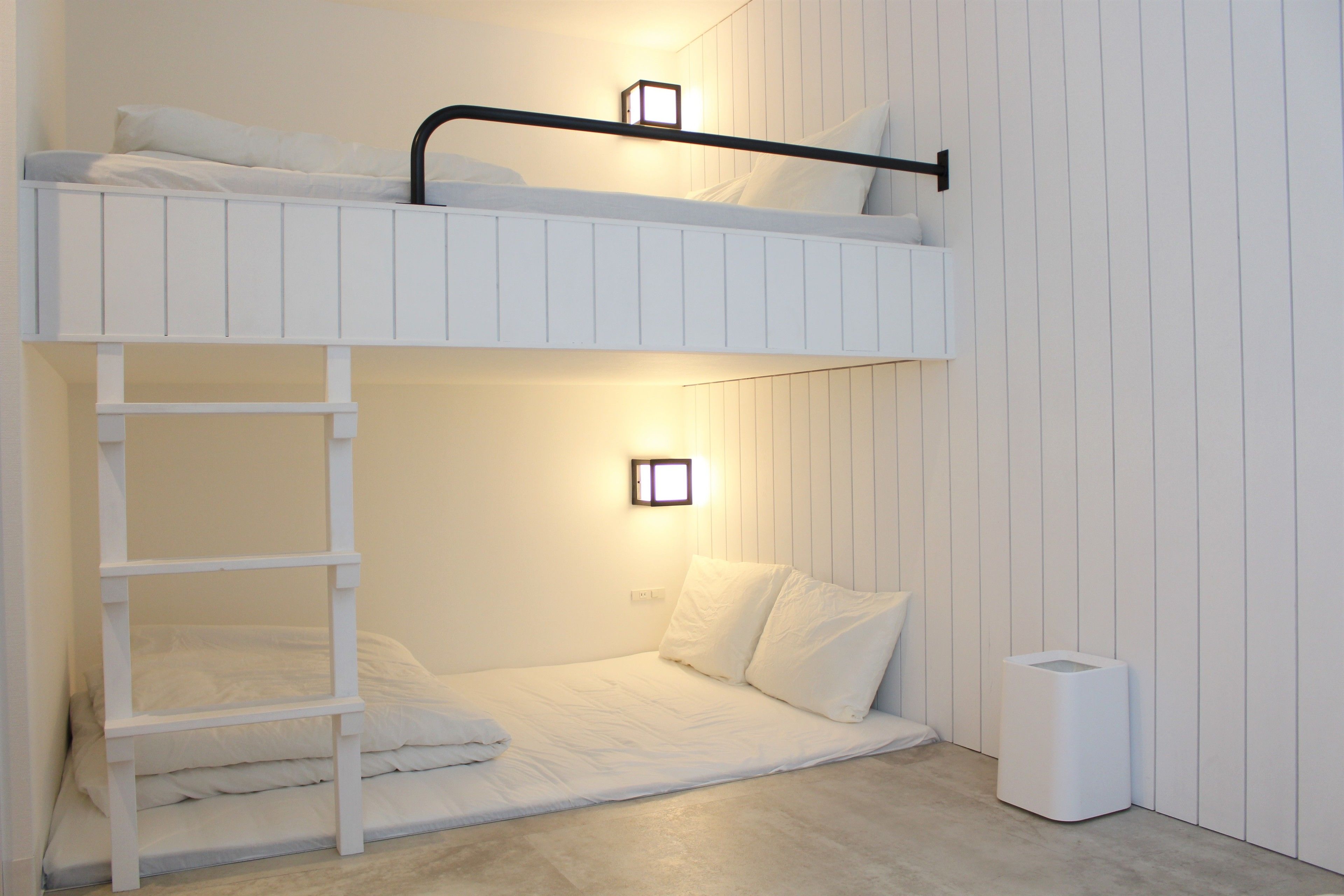 A bunk bed room with a ladder, a bedside table, and a wall-mounted light.