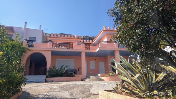A two-story building with a pink facade, a central entrance with steps, and a balcony with decorative railings.