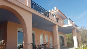 Un edificio de dos pisos con un balcón, una escalera y un jardín.