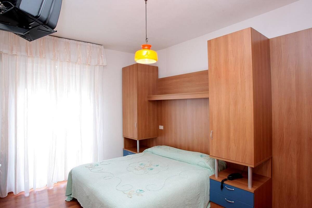 Un dormitorio con cama, armario de madera y lámpara colgante.
