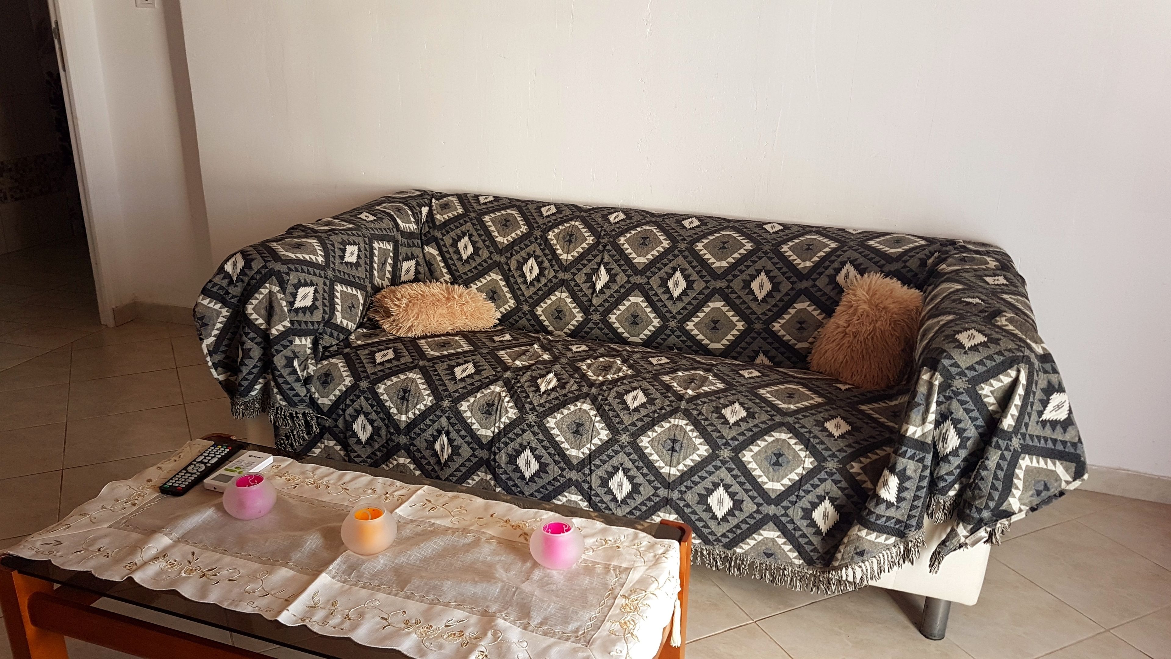 A sofa with a patterned cover, a table with a lace tablecloth, and two candles.