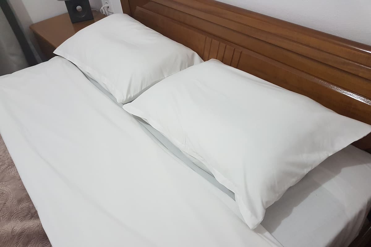 Ein ordentlich bezogenes Bett mit weißen Leinen und einem hölzernen Kopfteil.
