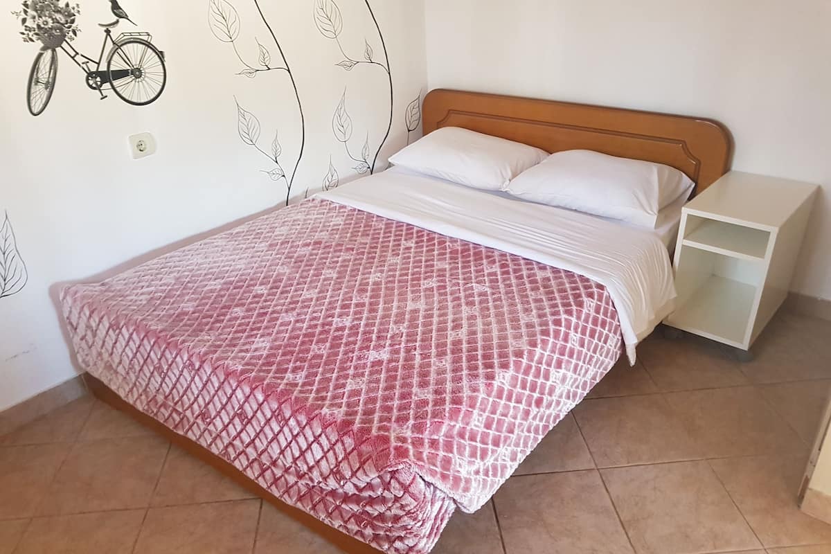 Ein Bett mit rosa kariertem Überwurf, einem Holz-Kopfteil, weißen Kissen und einem Nachttisch mit einer weißen Lampe.