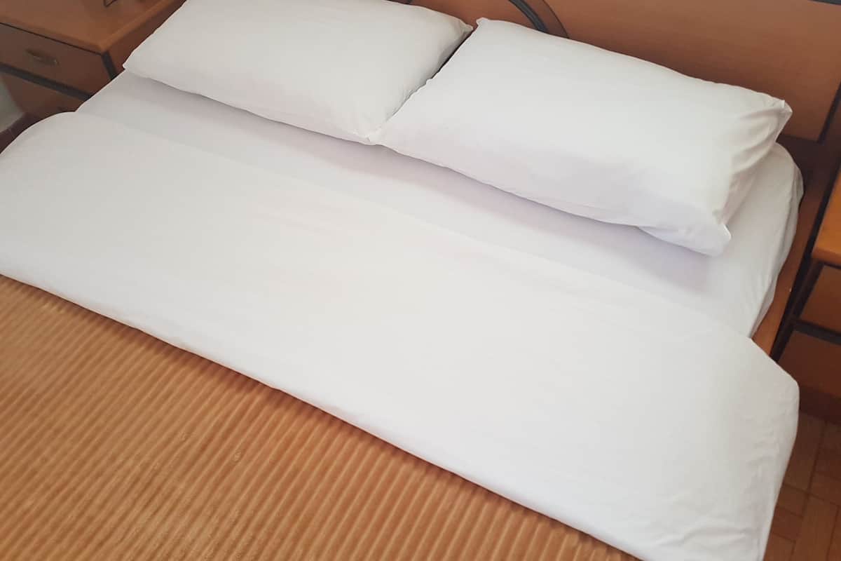 Ein ordentlich bezogenes Bett mit weißen Leinen in einem Zimmer mit Holzmöbeln und einem Metall-Kopfteil.