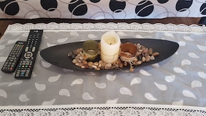 A table with a lace tablecloth, a candle, a plate with pebbles, and two remote controls.